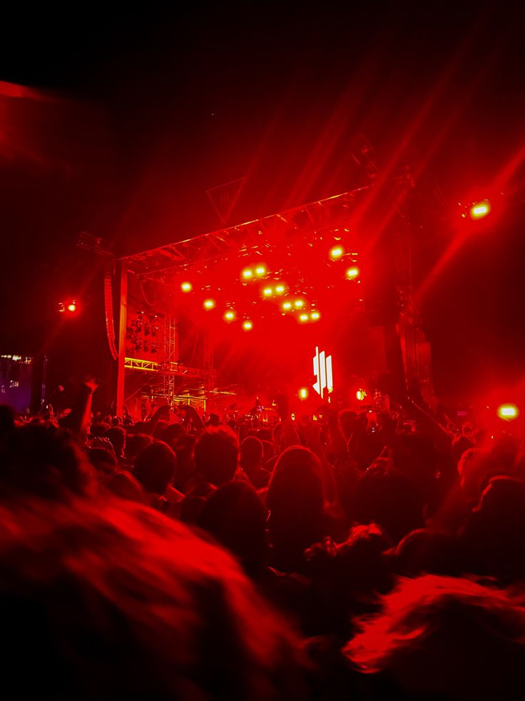 a large group of people standing on top of a stage with red lights in the dark