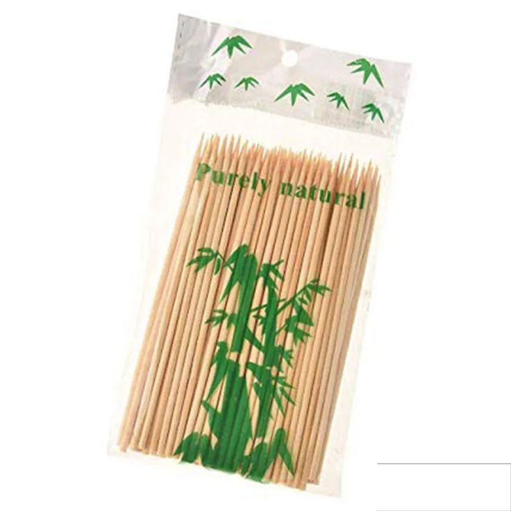 bamboo sticks with green leaves on them in a plastic bag, sitting on top of a white surface