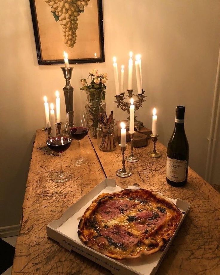 a pizza sitting on top of a wooden table next to wine bottles and candles in a room