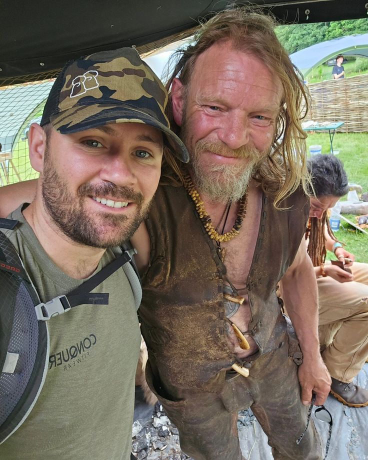 two men standing next to each other in front of a tent