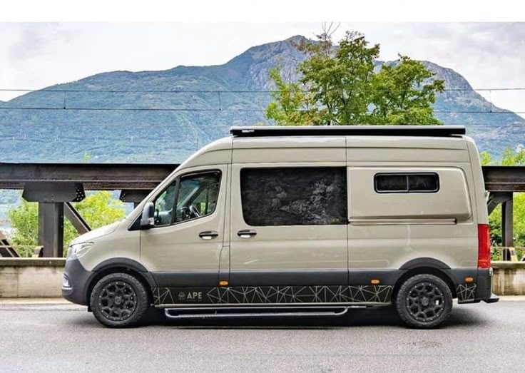 a white van parked on the side of a road next to a bridge with mountains in the background