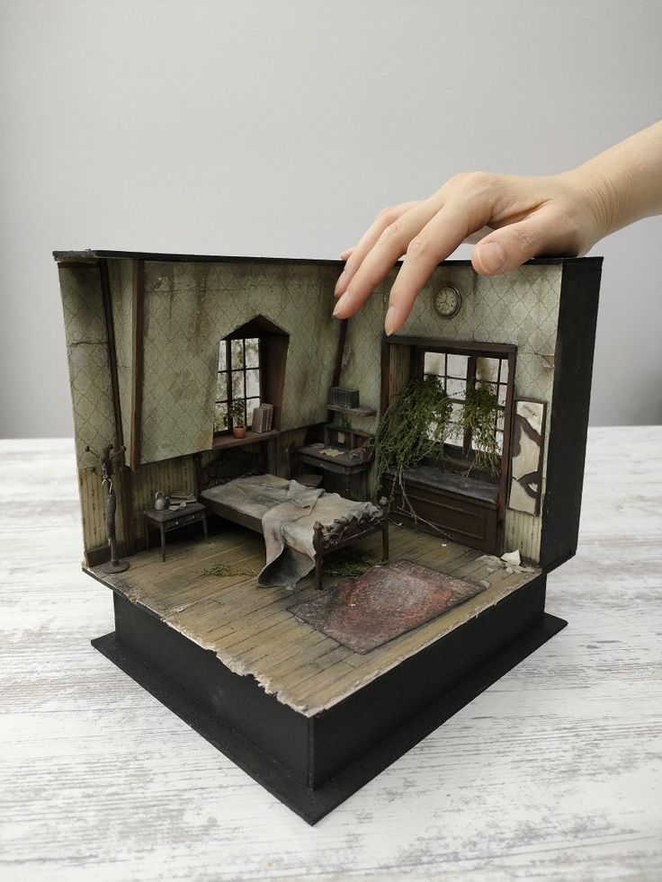 a hand is reaching for the inside of a doll house that has been placed on a table