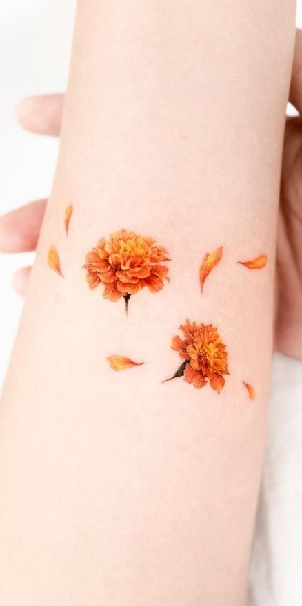 an orange flower on the side of a woman's arm with petals scattered around it