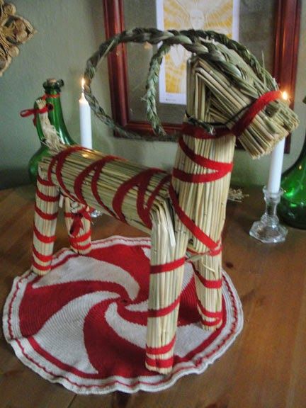 a wooden rocking horse made out of straw wrapped in red and white ribbon with candles on the side