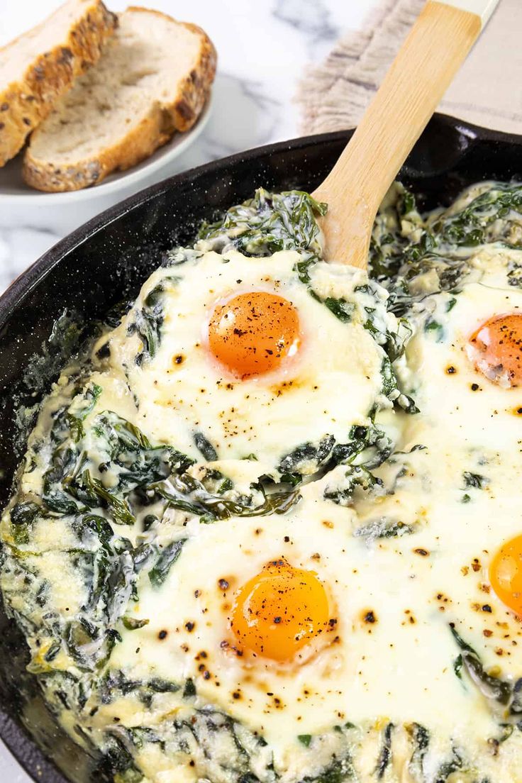 three eggs in a skillet with spinach and bread on the side next to it