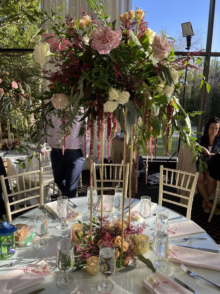 a tall vase filled with lots of flowers on top of a white table cloth covered table