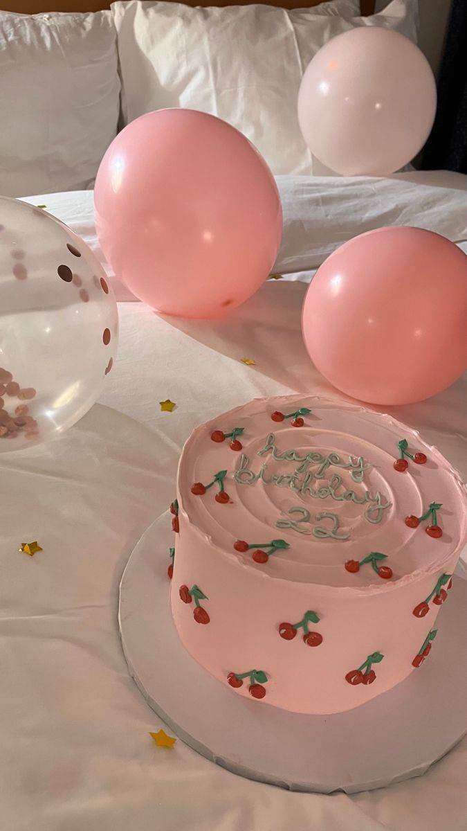 a pink cake on a table with balloons and confetti