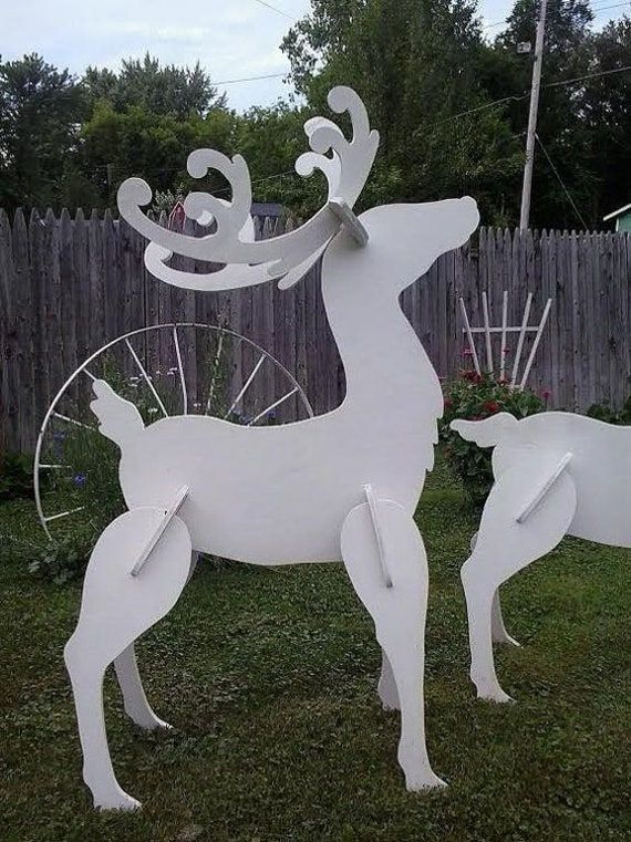 two white deer sculptures in the grass near a fence