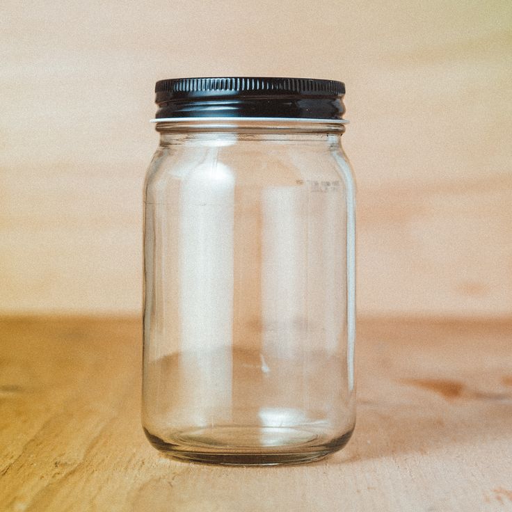 a clear glass jar sitting on top of a wooden table next to a black lid