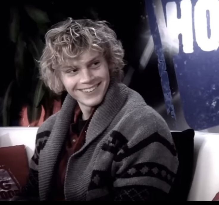 a young man sitting on top of a white couch next to a potted plant