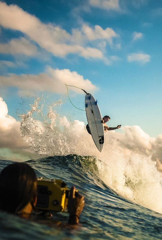 a man riding a surfboard on top of a wave in the ocean next to a camera