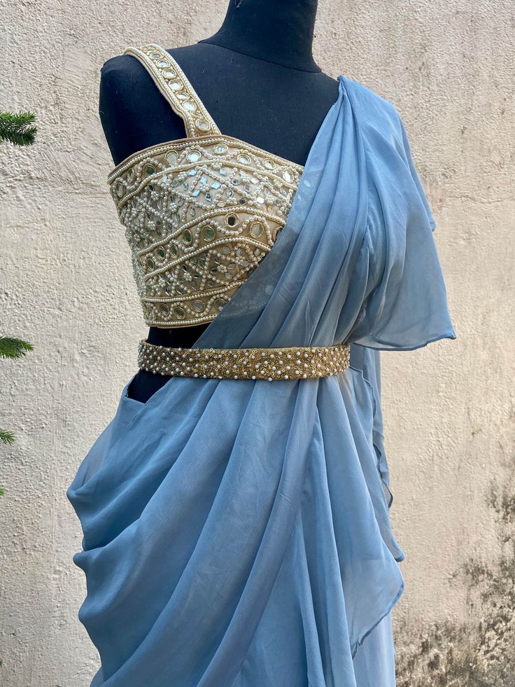 A two-piece blue ruffle saree set from the Priti Sahni collection. This beautiful blue georgette draped ruffle saree is paired with our classic mirror and pearl hand embroidered bustier blouse. The blouse has mirror-sequin tassels tie-up at the back. The outfit is completed with a heavy embroidered pearl belt.
Belt Included. Pre-draped Georgette Lehenga For Designer Wear, Pre-draped Georgette Lehenga, Pre-draped Fitted Lehenga In Georgette, Fitted Georgette Lehenga In Pre-draped Style, Blue Draped Fitted Choli, Fitted Chiffon Pre-draped Saree With Ruffles, Blue Fitted Draped Choli, Fitted Draped Blue Choli, Blue Choli With Ruffles And Traditional Drape