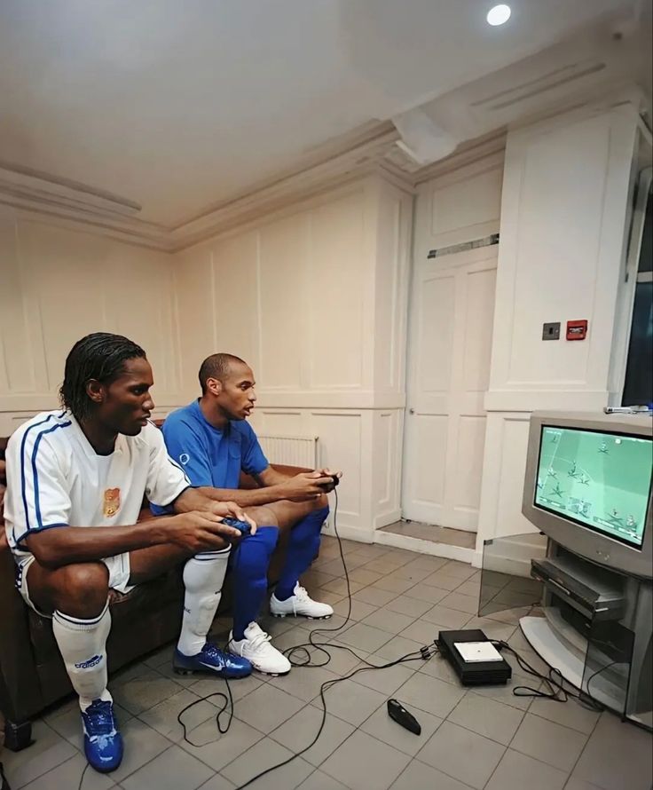 two men sitting in front of a tv playing video games with remote controllers on the floor