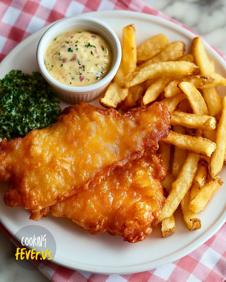 a white plate topped with fish and fries next to a bowl of sauce on top of a checkered table cloth