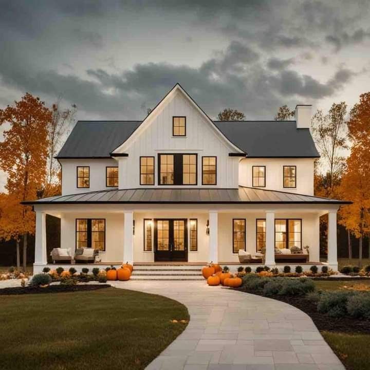 a white house with lots of windows and pumpkins on the front lawn at dusk