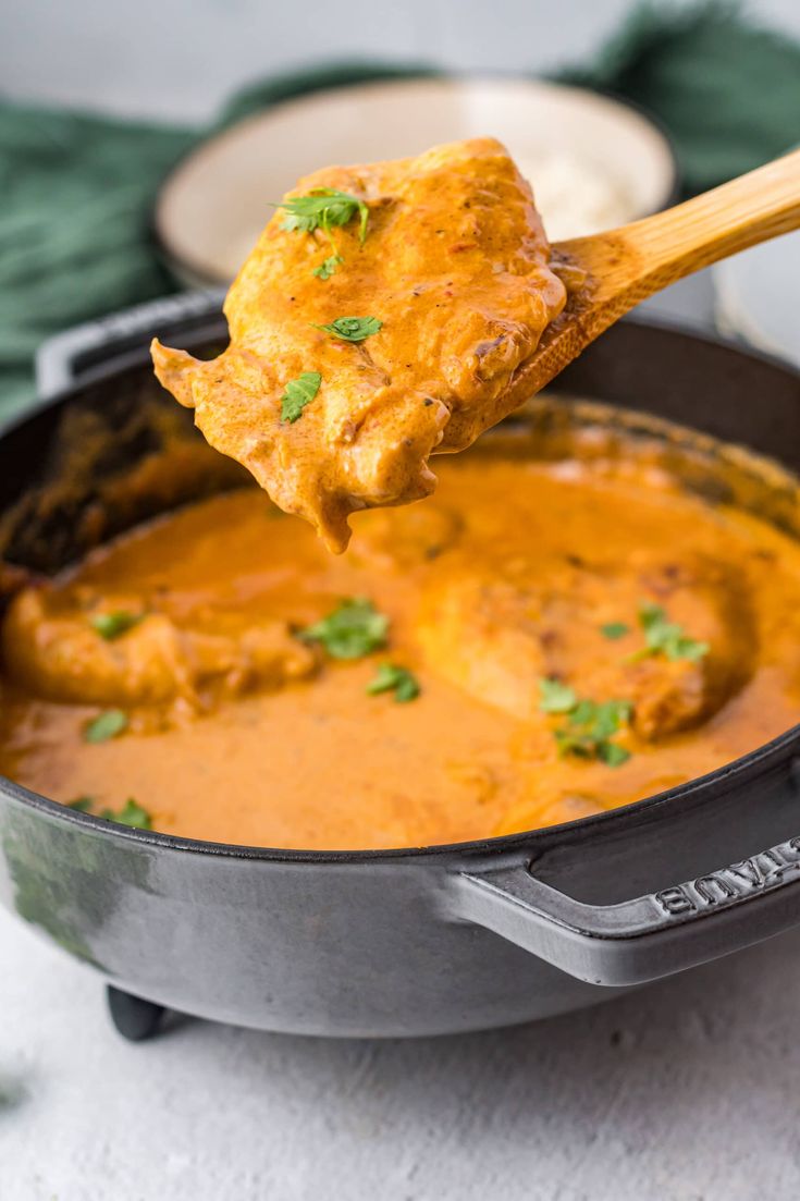 a wooden spoon full of curry being lifted from a skillet with meat in it