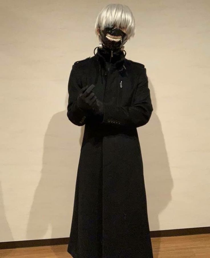 a man in a black coat and mask standing next to a wall