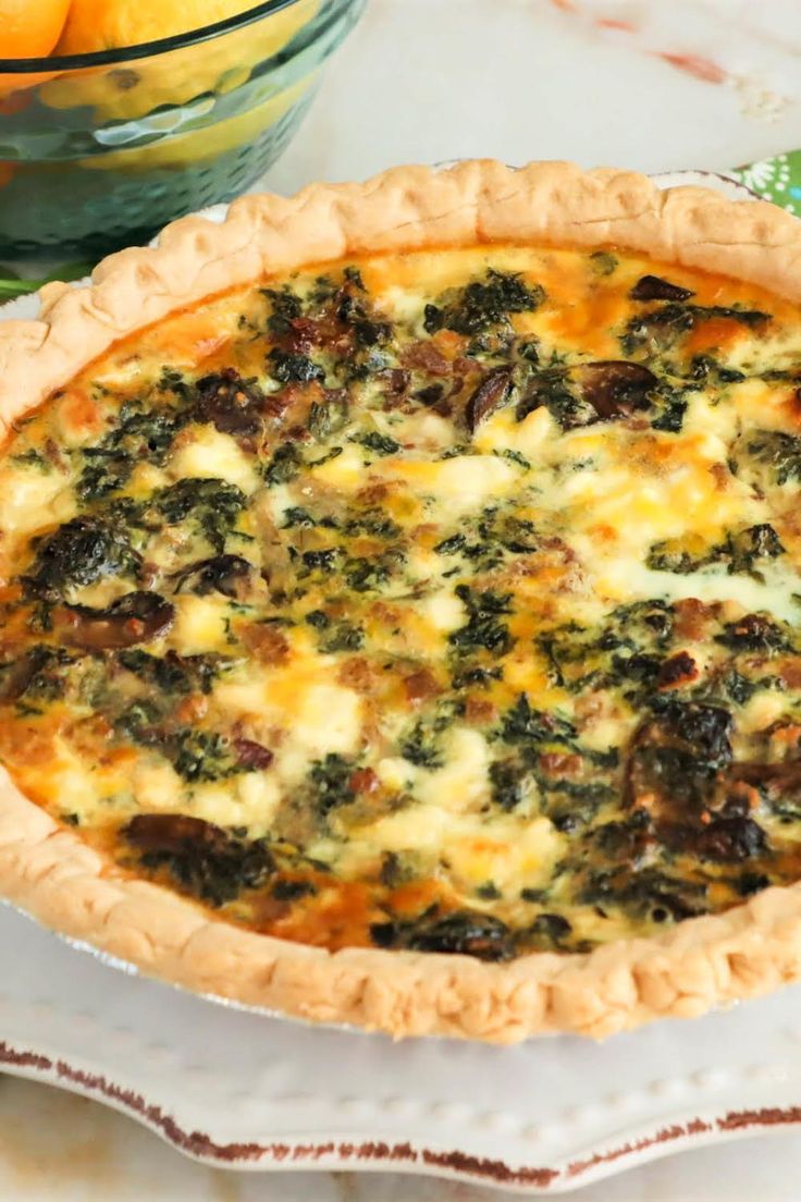 a quiche with cheese and spinach in a pie pan next to oranges