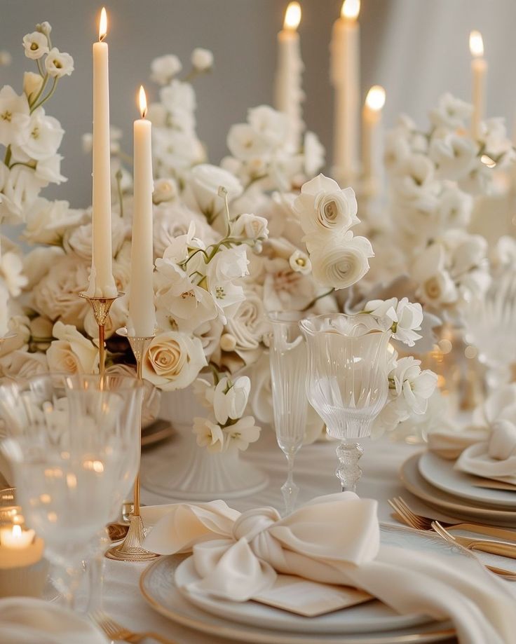 the table is set with white flowers and gold place settings, candles in the background