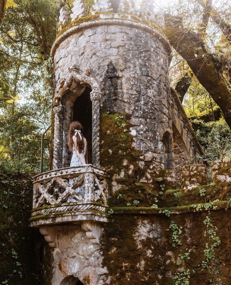 a woman in a white dress standing on a balcony next to an old stone building