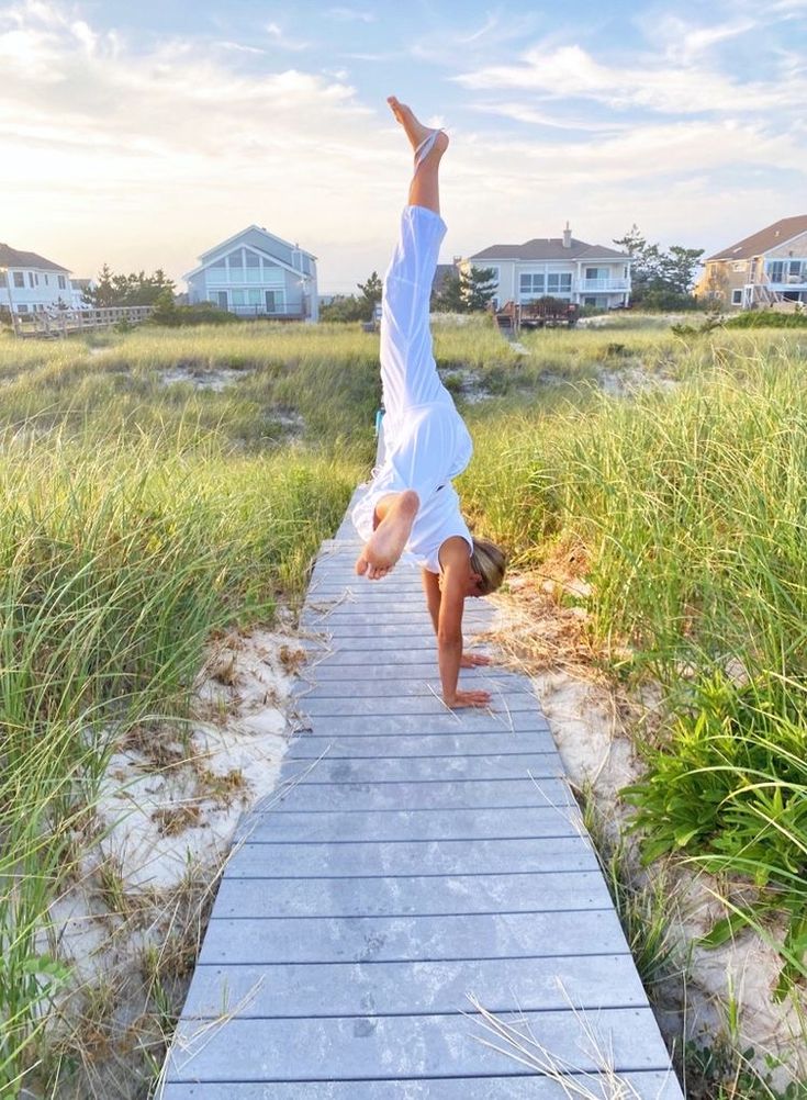 a person doing a handstand on a boardwalk in front of some grass and houses