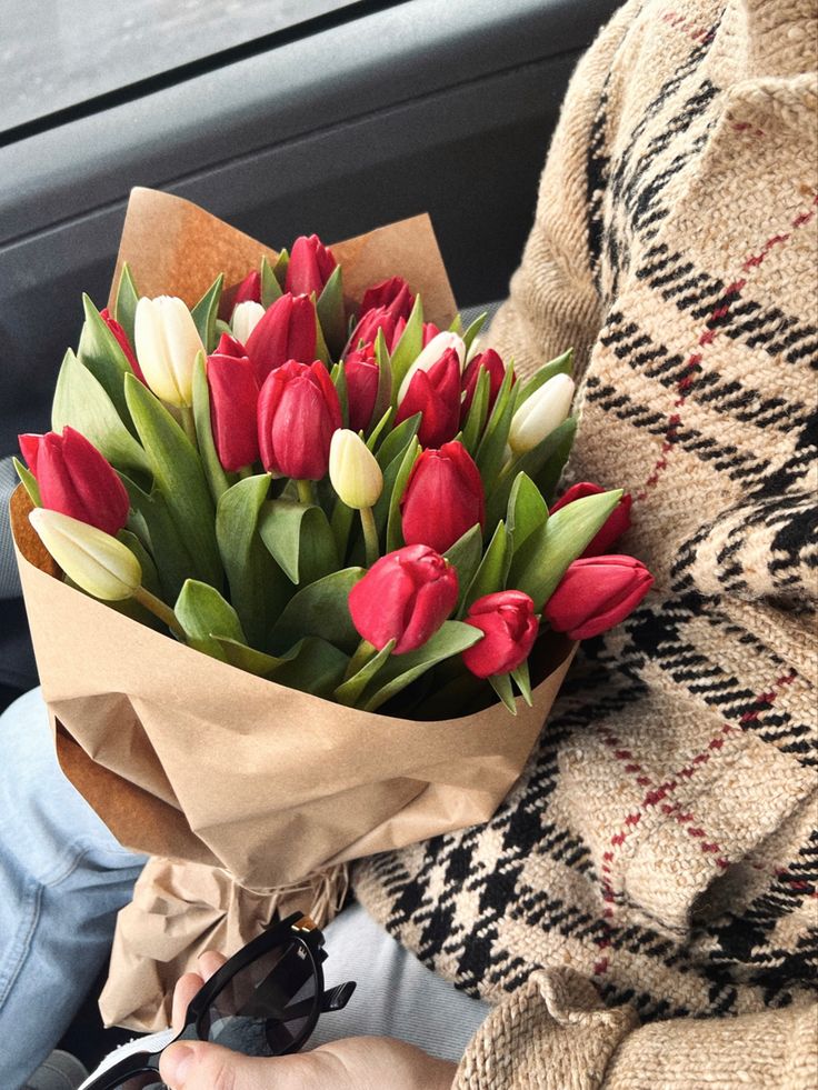 a person holding a bouquet of red and white tulips in their hand while sitting in a car