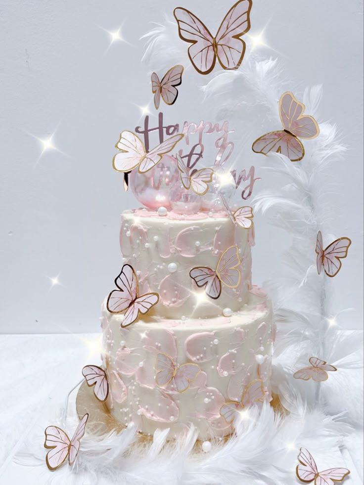 a three tiered cake with pink frosting and butterflies on top, surrounded by white feathers