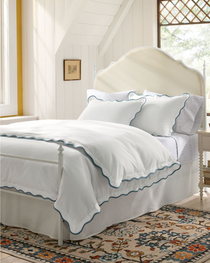 a bed with white sheets and blue trim on the headboard is in a bedroom