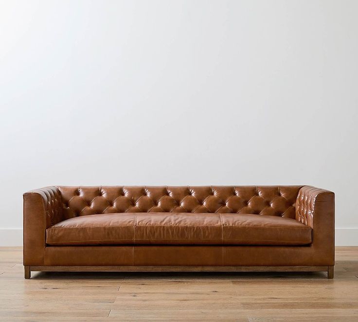 a brown leather couch sitting on top of a hard wood floor next to a white wall