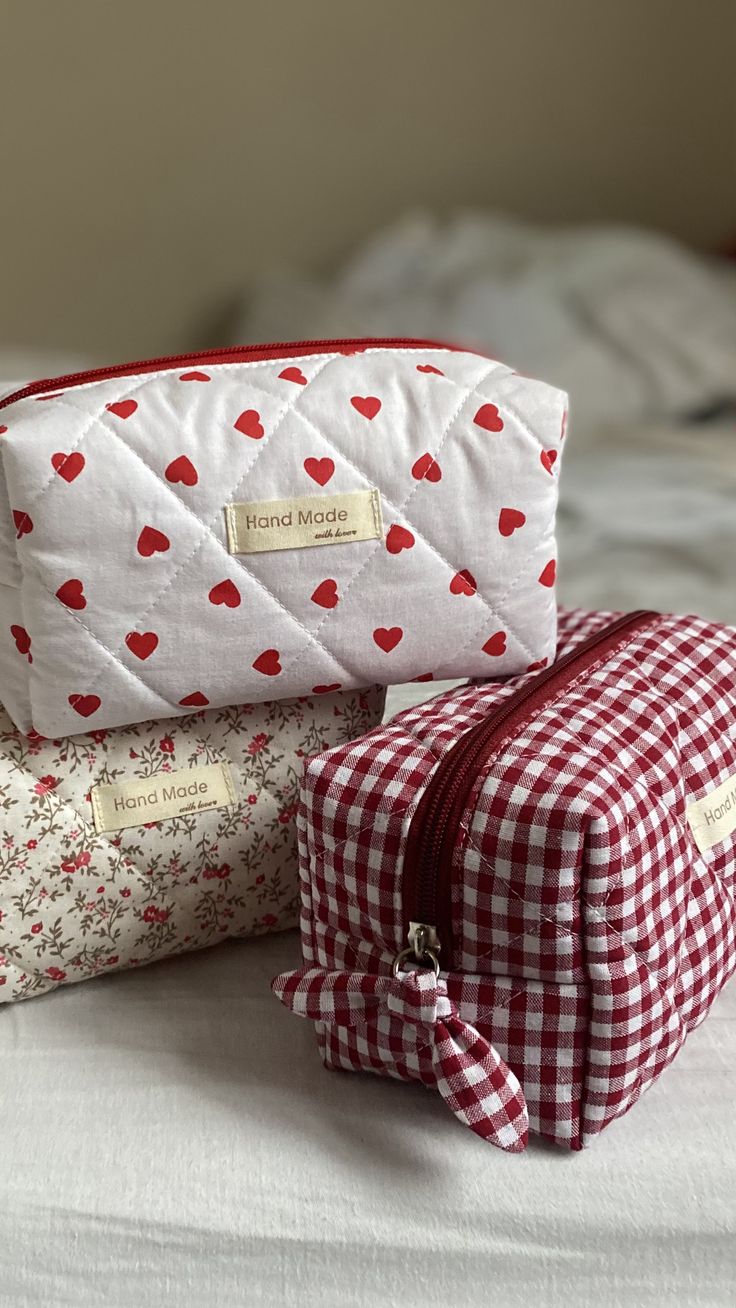 two cosmetic bags sitting on top of a bed covered in red and white checkered fabric