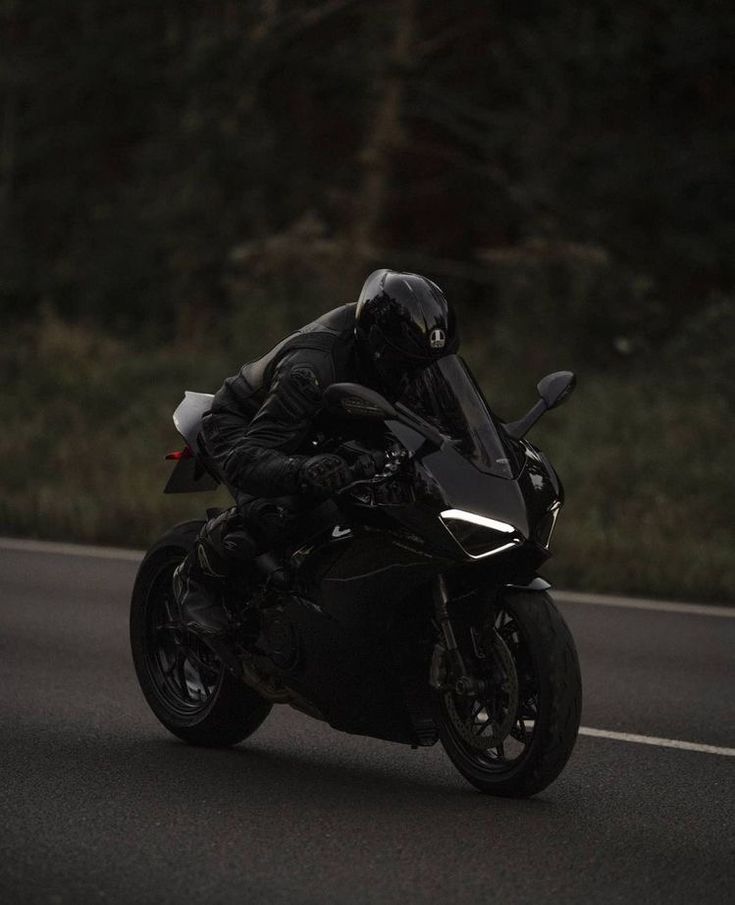 a man riding on the back of a black motorcycle down a curvy road