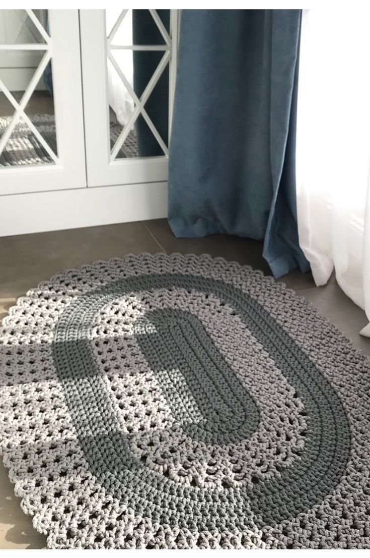 a gray and white crocheted rug sitting on top of a floor next to a window