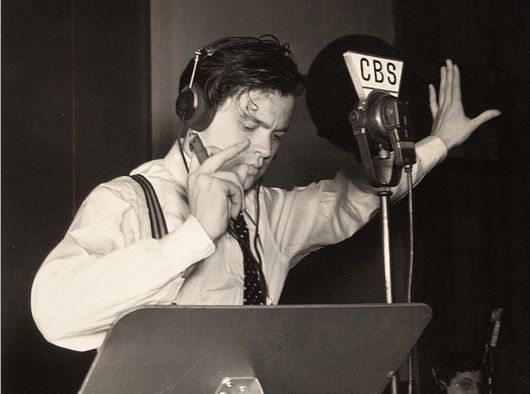 a man wearing headphones standing in front of a microphone and holding his hand up to his ear