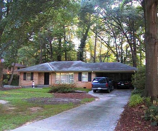 a car is parked in front of a house with trees around it and grass on the ground