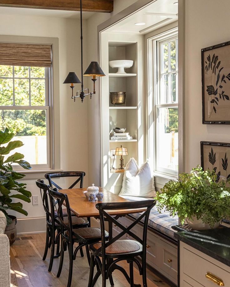 a dining room table and chairs in front of a window with potted plants on it