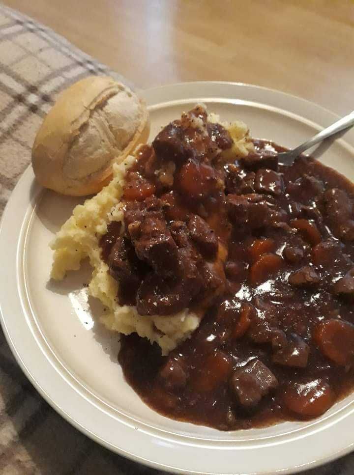 a white plate topped with mashed potatoes covered in beef and gravy next to a roll