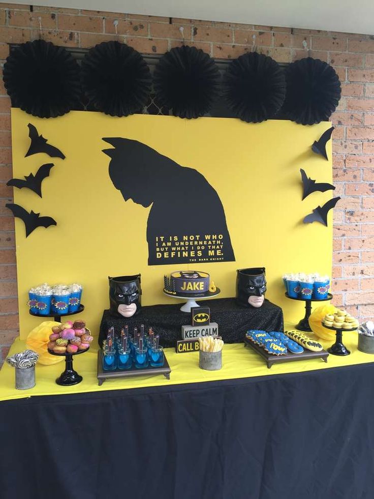 a batman themed dessert table with cupcakes and cake on the table in front of it