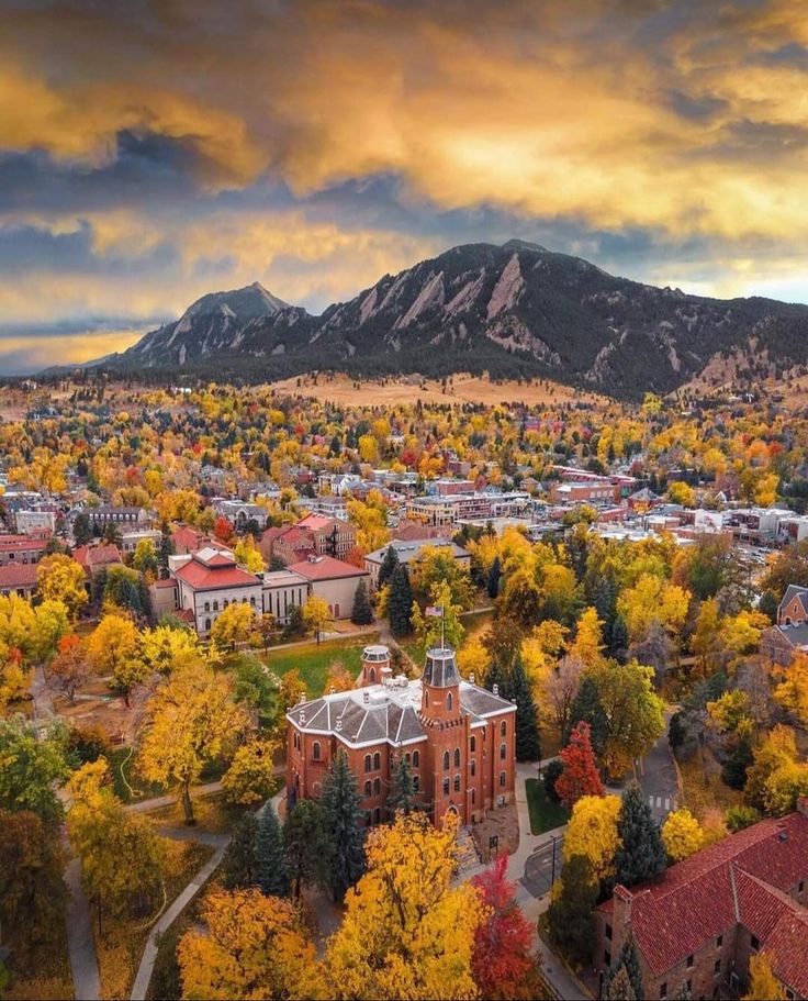 an aerial view of a city with mountains in the background and autumn foliage around it