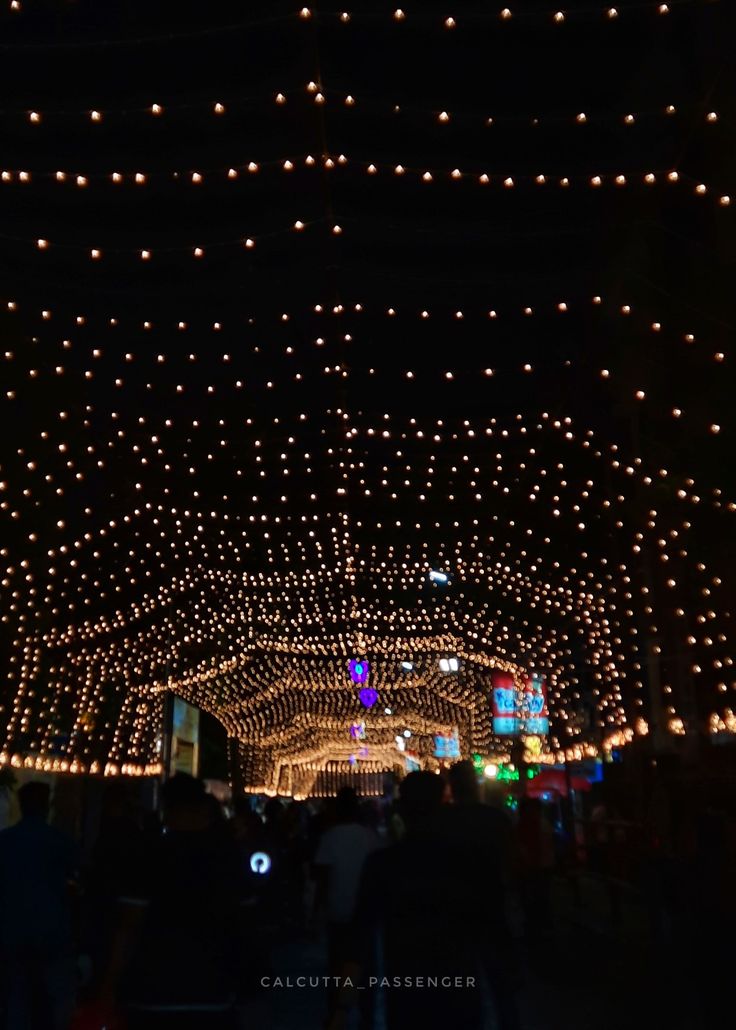 people are walking through the tunnel covered in lights