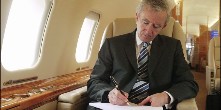 a man in a suit and tie writing on a piece of paper next to an airplane window