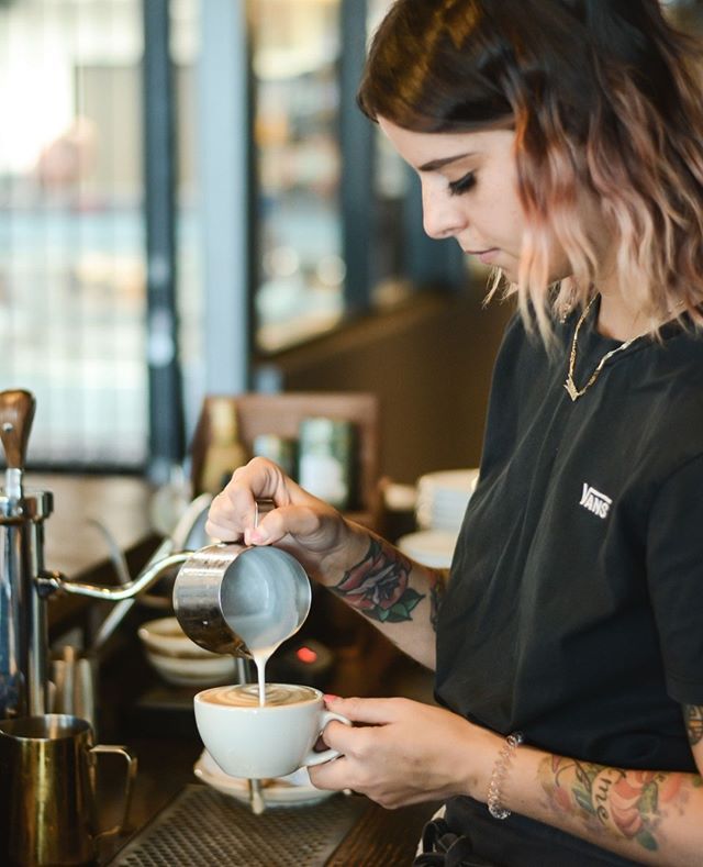 a woman pouring coffee into a white cup