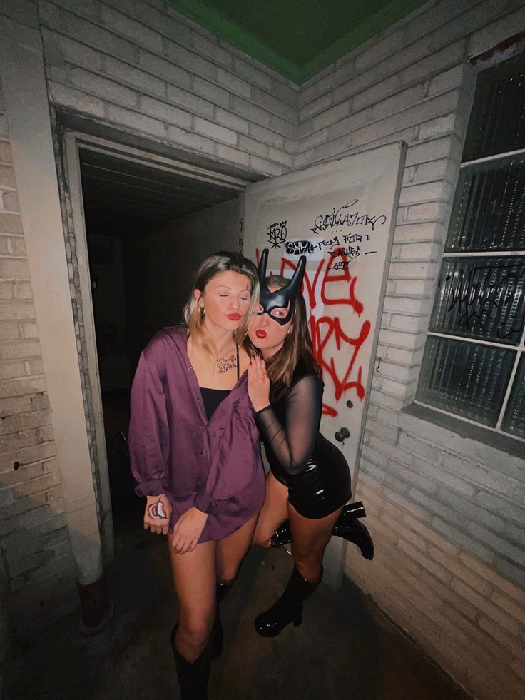 two women dressed up as batman and catwoman posing for the camera in an alleyway