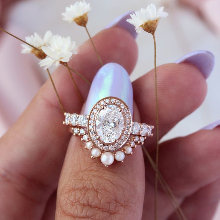 a close up of a person holding a ring on their finger with flowers in the background