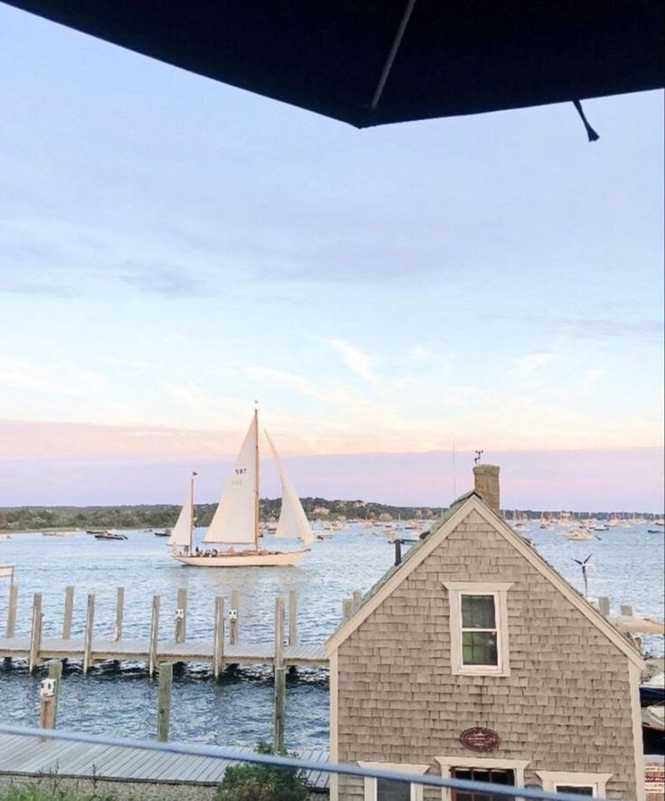 a sailboat is out on the water near a house and dock with a boat in the distance