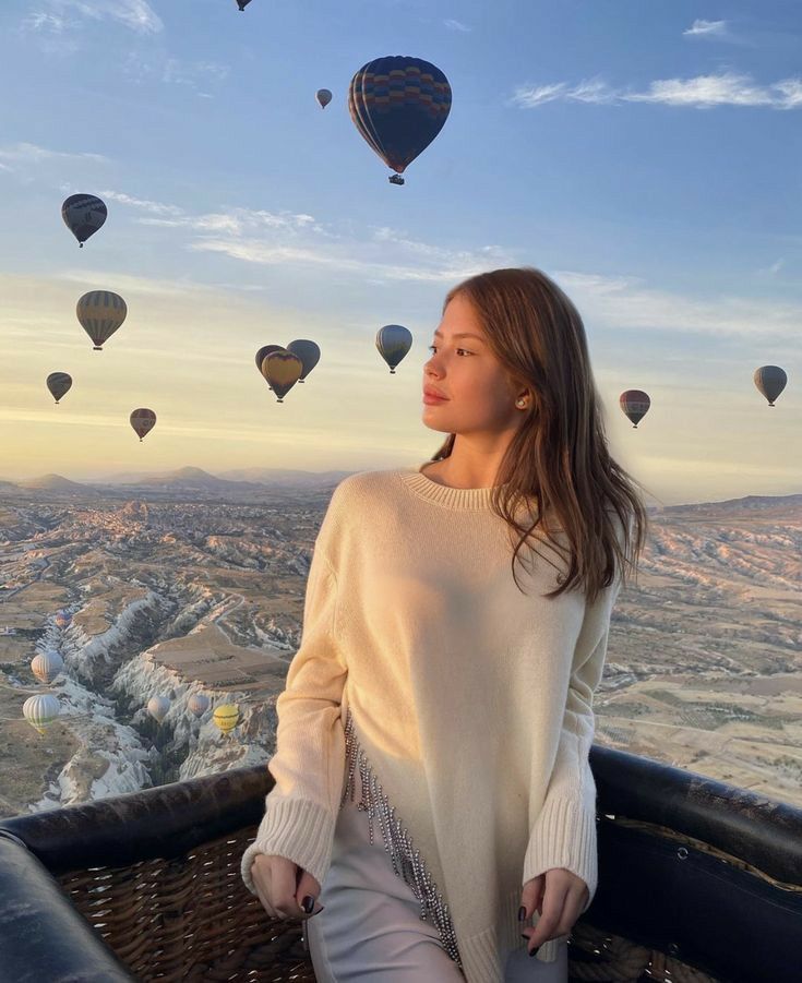 a woman sitting on top of a hot air balloon in the sky with balloons flying above her