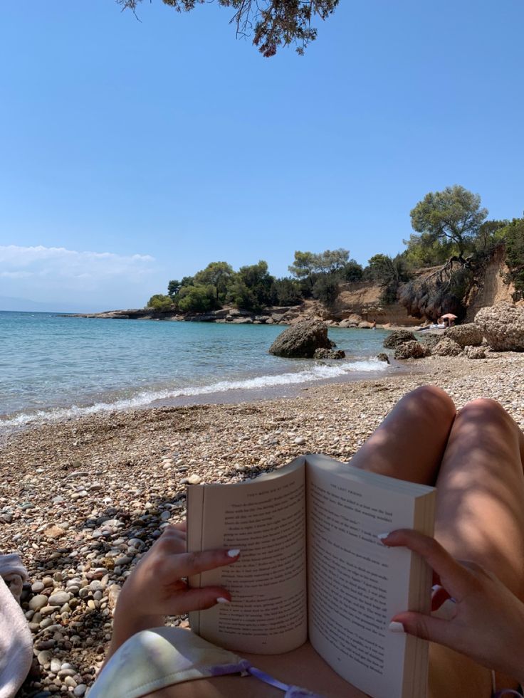 a woman laying on the beach reading a book