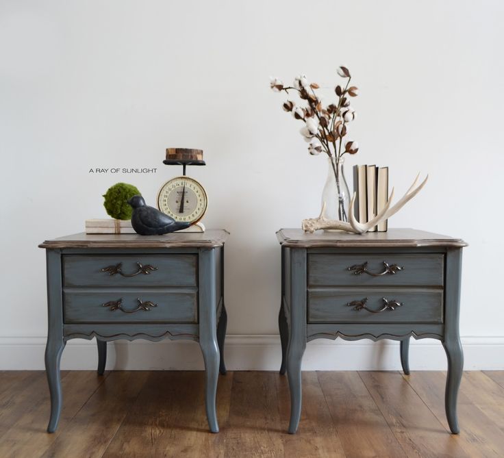 two gray nightstands with books and flowers on them in front of a white wall