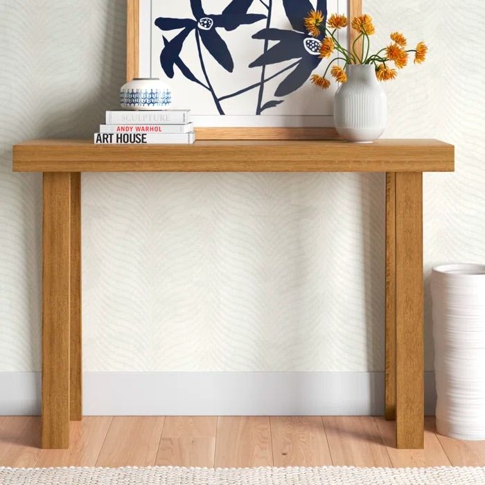 a wooden table topped with a white vase filled with flowers next to a framed art piece