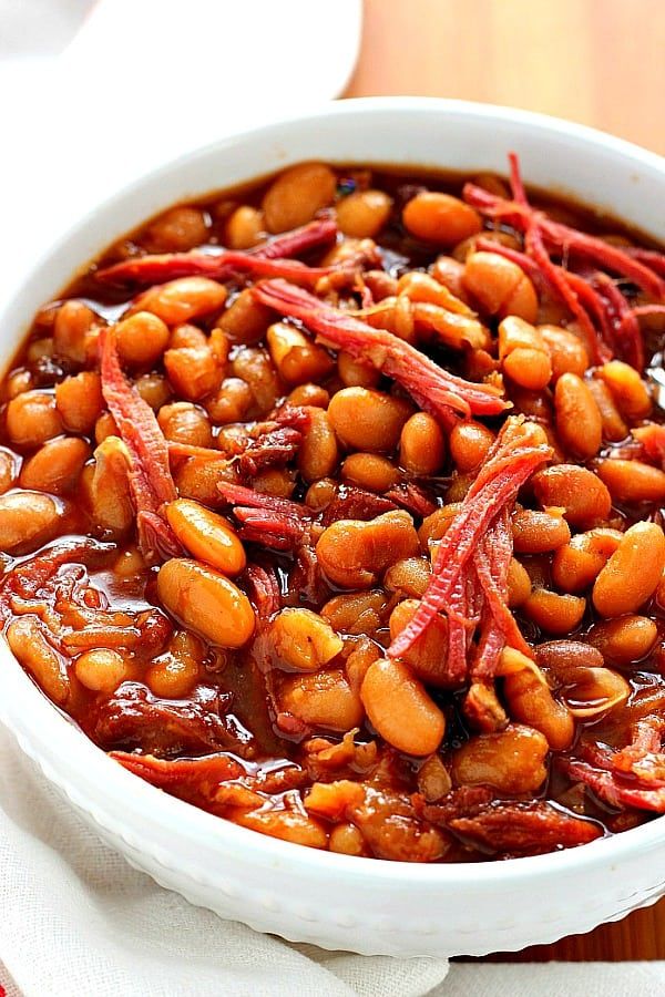 a white bowl filled with beans on top of a wooden table next to a napkin