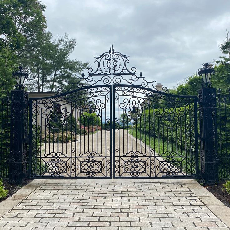 an iron gate in front of a brick driveway